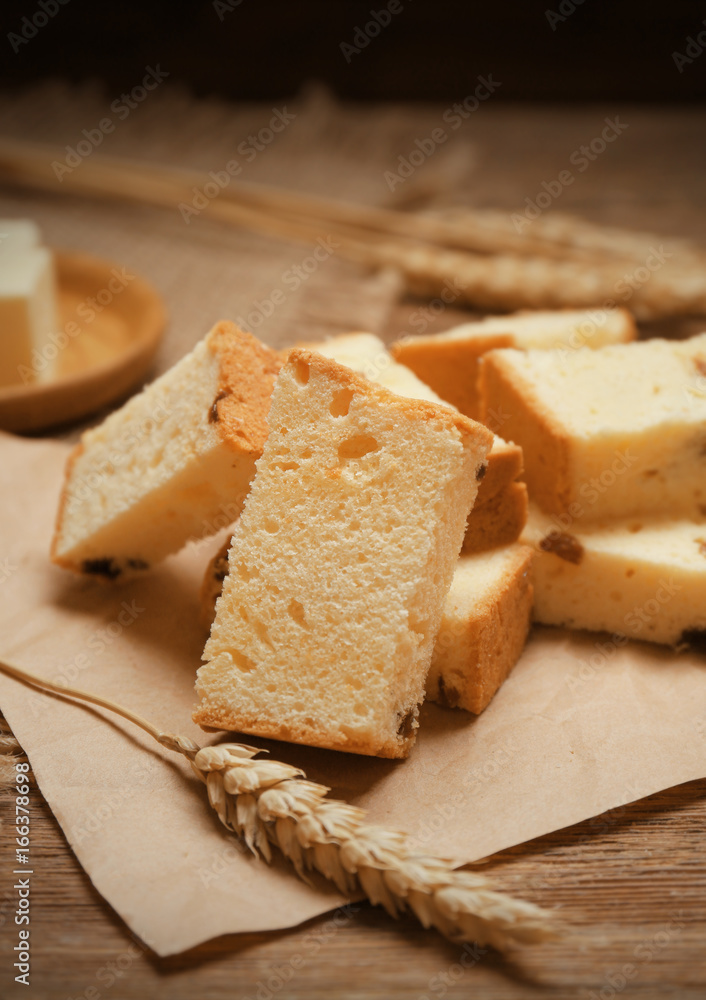 Paper with delicious butter cake and wheat ear on wooden table