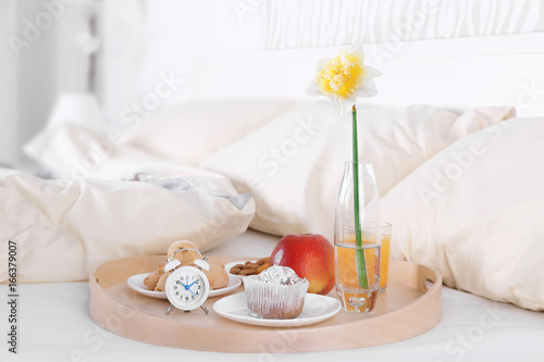 Wooden tray with tasty breakfast on bed