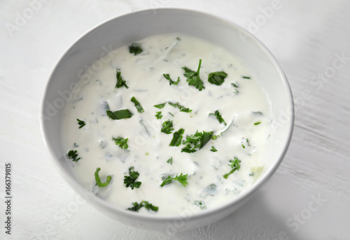 Bowl with delicious sauce and herbs on white wooden background, closeup