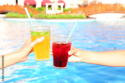 Hands of young women clinking glasses with cocktails near pool