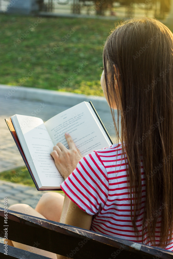 Obraz premium Back view of a young woman reading a book and relaxing in the park