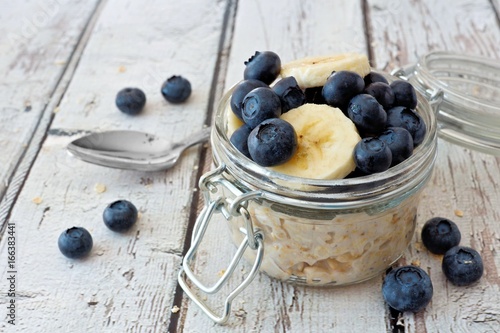 Overnight oats with fresh blueberries and bananas in a jar on a rustic white wood background