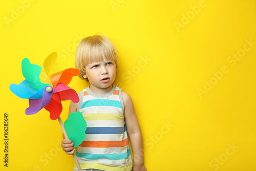 Portrait of little boy with rainbow whirligig on yellow background