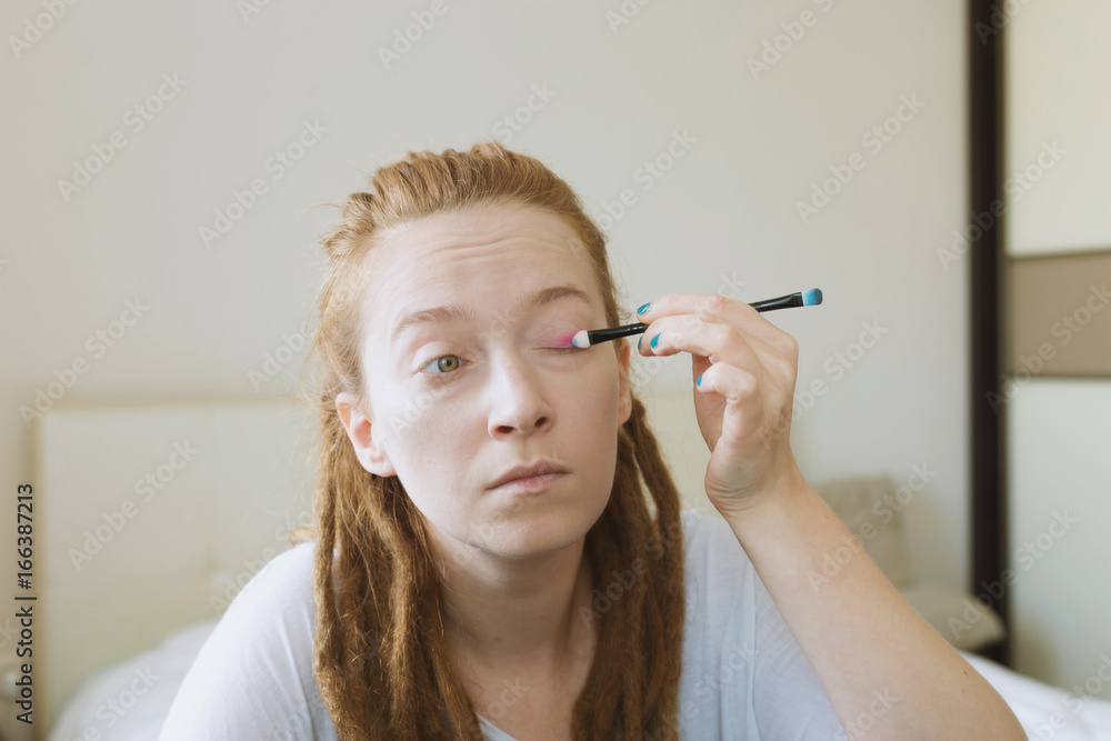 Ginger woman with dreadlocks is making up herself in front of the mirror in bedroom Ginger woman with dreadlocks is making up herself in front of the mirror in bedroom