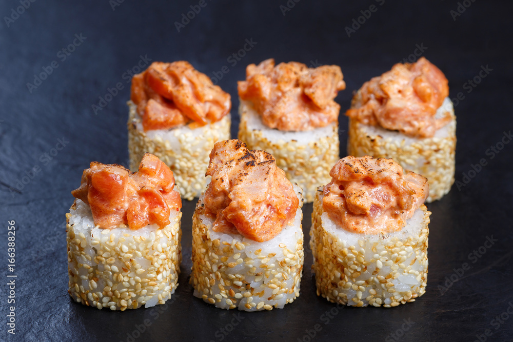 Sushi rolls topped with torched salmon served on black stone slate. Restaurant menu, Japanese food art.