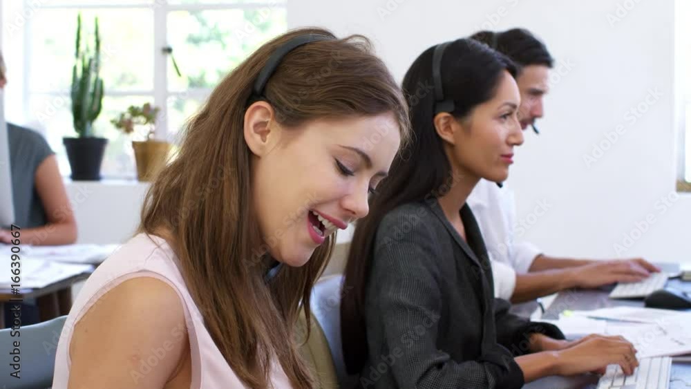 White woman in headset smiles to camera in open plan office White woman in headset smiles to camera in open plan office