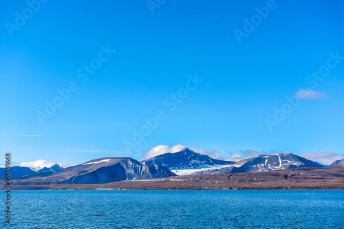landscape of the Arctic Ocean and reflection with blue sky and mountains with snow on a sunny day, Norway, Spitsbergen, Longyearbyen, Svalbard, summer