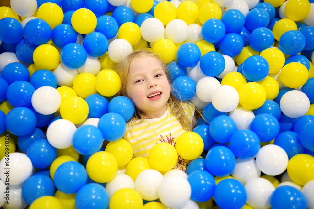 Obraz premium Happy little girl having fun in ball pit in kids indoor play center. Child playing with colorful balls in playground ball pool.