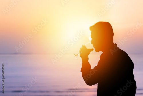 Photography Silhouette of man drinking wine in glass at sunset at the beach