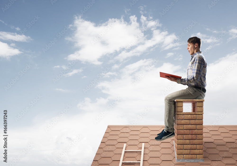 Handsome man on brick roof against cloud scape reading book Handsome man on brick roof against cloud scape reading book