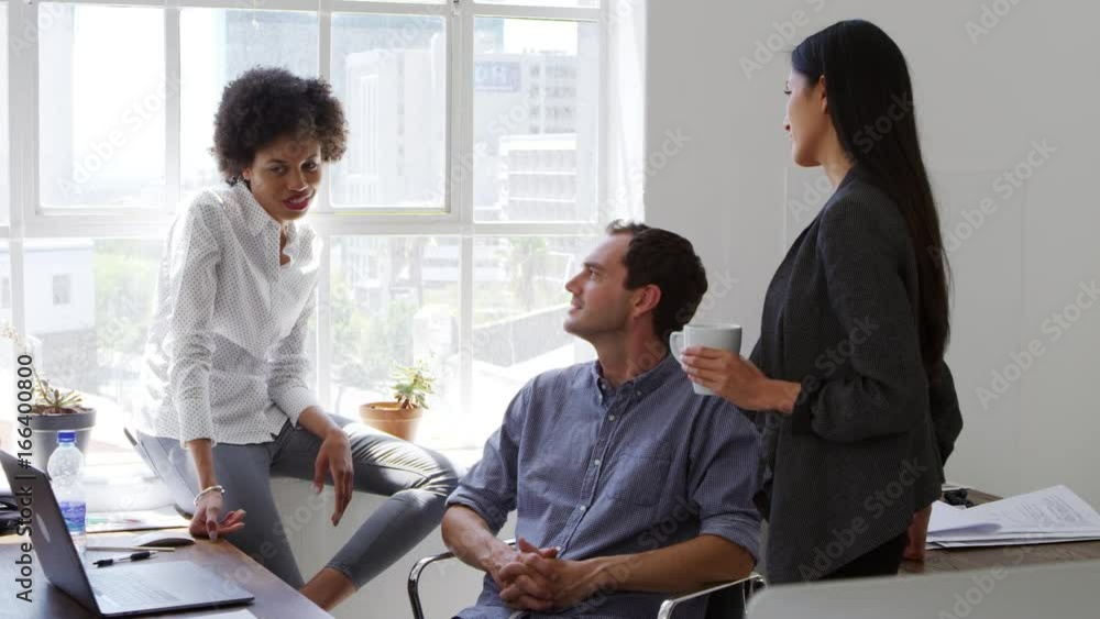 Young man and two female colleagues talking in an office Young man and two female colleagues talking in an office