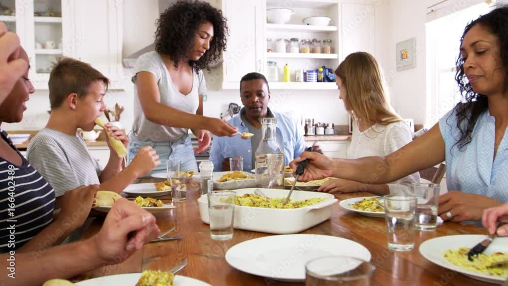 Two Families With Teenage Children Eating Meal In Kitchen Two Families With Teenage Children Eating Meal In Kitchen