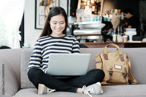 Beautiful asian girl using laptop computer while sitting on sofa with smiling face emotion, people and technology concept, lifestyle © mangpor2004