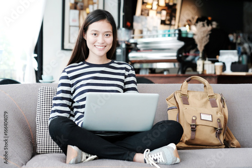 Beautiful asian girl using laptop computer while sitting on sofa with smiling face emotion, people and technology concept, lifestyle © mangpor2004