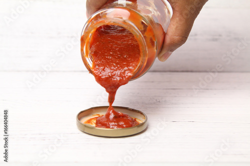 Hand pour delicious homemade classic spicy tomato pasta or pizza sauce over wooden texture background. Selective Focus