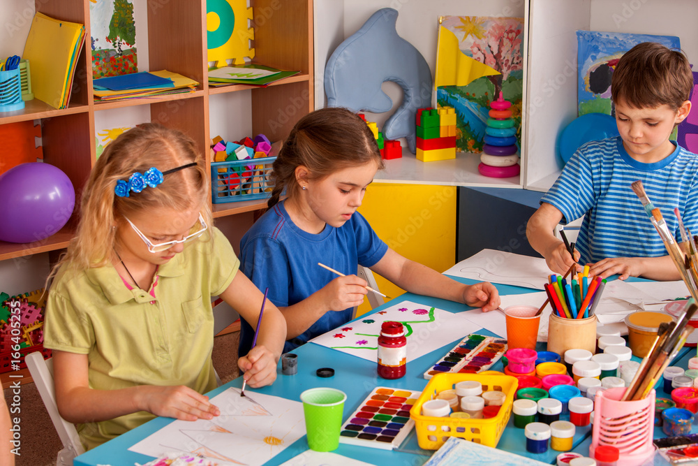 Fototapeta premium Small students girls painting in art school class. Children boy and girl drawing by paints on table. Children have fun at the children's club. Preparing for a school exhibition of plasticine.