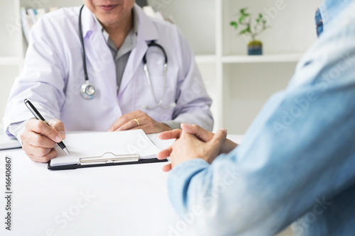 patient listening intently to a male doctor explaining patient symptoms or asking a question as they discuss paperwork together in a consultation