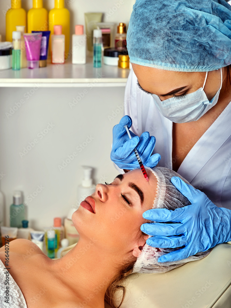 Filler injection for woman forehead face. Plastic aesthetic facial surgery by doctor in beauty clinic. Doctor in medical gloves with syringe. Skin tightening. Cosmetics in bottles in the background.