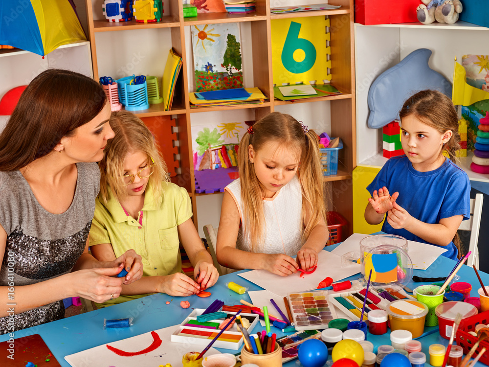 Fototapeta premium Plasticine modeling clay in children class. Teacher teaches kids together play dough and mold from plasticine in kindergarten or preschool. Collective creativity. Zoo from plasticine.