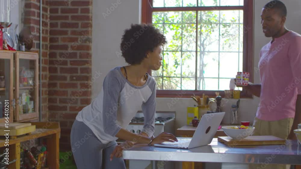 Mixed race couple using laptop computer talking in kitchen, shot on R3D Mixed race couple using laptop computer talking in kitchen, shot on R3D