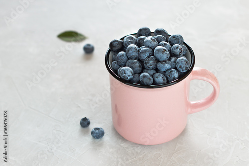 Fresh blueberries in pink mug or cup on light gray background. photo