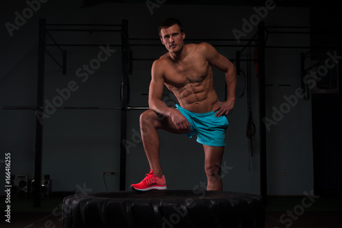 Confident young man with hummer and tire in gym