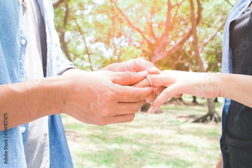 Man putting engagement silver ring on woman hand, outdoor, Green garden with bokeh