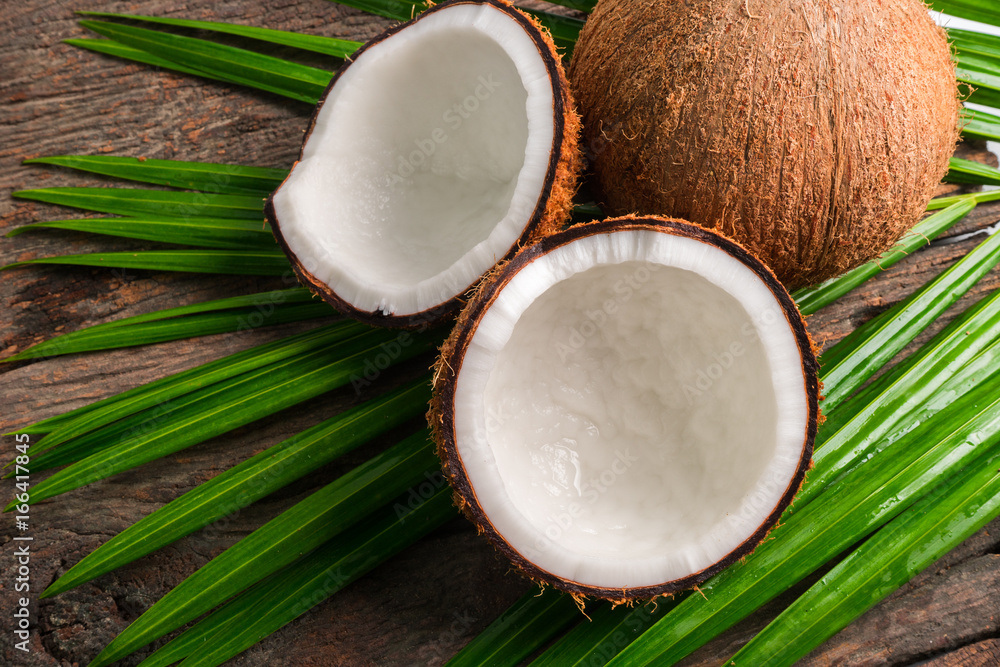 Coconut halves and green leaf on old wood background. Top view with copyspace Coconut halves and green leaf on old wood background. Top view with copyspace