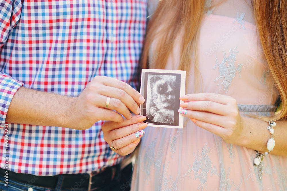 Close up of pregnant woman holding ultrasound scan on her tummy. Ultrasound of baby in mother's womb. Close up of pregnant woman holding ultrasound scan on her tummy. Ultrasound of baby in mother's womb.