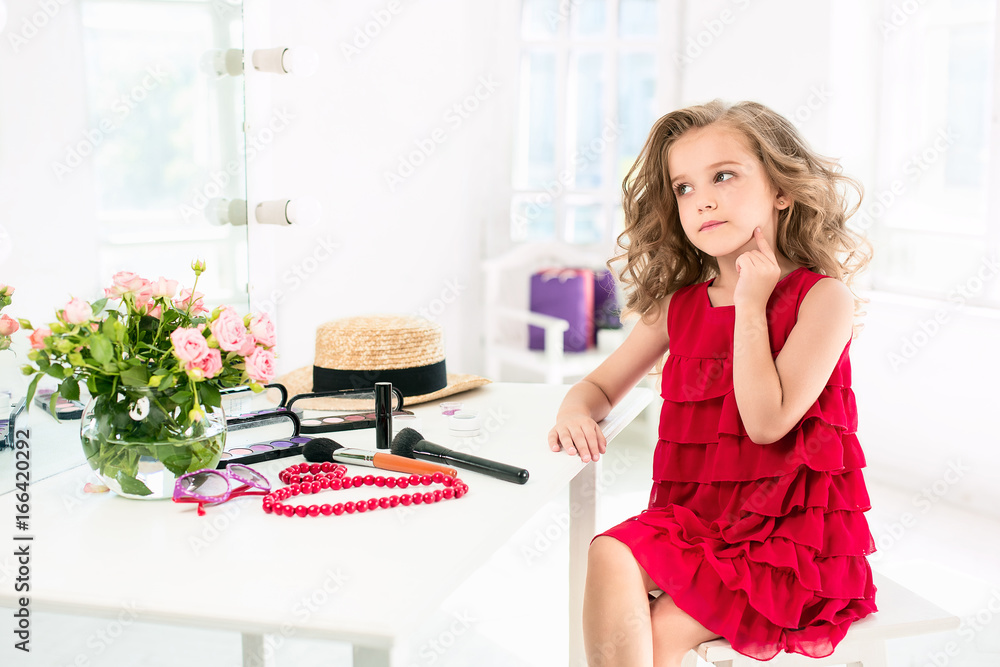 A little girl with cosmetics. She is in mother's bedroom, sitting near the mirror. A little girl with cosmetics. She is in mother's bedroom, sitting near the mirror.