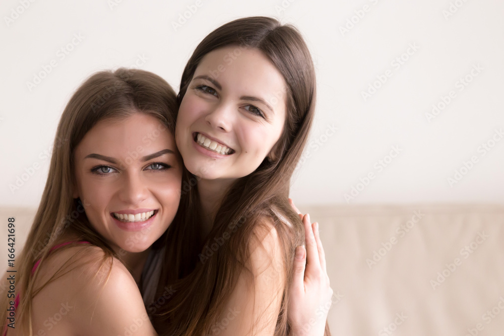 Close up headshot portrait of smiling young female friends warmly embracing during meeting. Two happy young women hugging and looking in camera. Strong friendship and sincere feelings between people