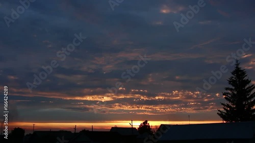 Colorful cloudy sky decline in the silent evening at village. Locust chirring around. Dark rural roofs panning. No people. photo