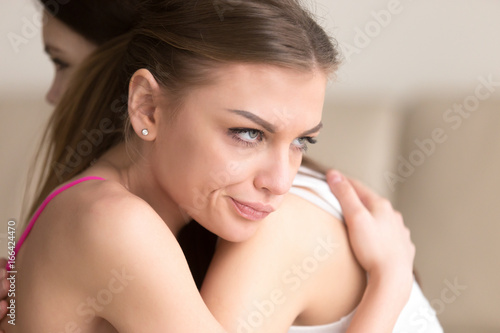 Fotografia Young woman with dissatisfied and angry facial expression embracing girlfriend, insincere female hiding her envy or jealous, thinking about deception