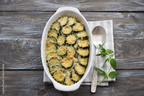 Gratin zucchini with cheese and greens on a wooden background. Delicious homemade food photo