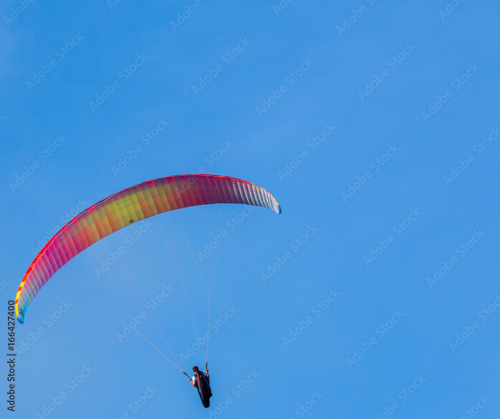 Orange and yellow paraglider on clear blue sky Orange and yellow paraglider on clear blue sky
