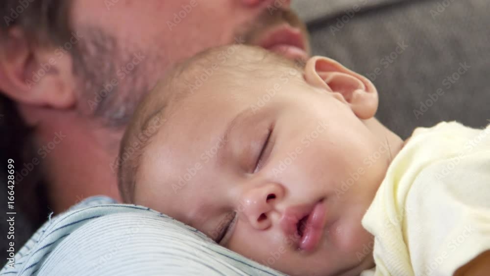Close Up Of Father Sitting On Sofa Holding Sleeping Baby Son Close Up Of Father Sitting On Sofa Holding Sleeping Baby Son