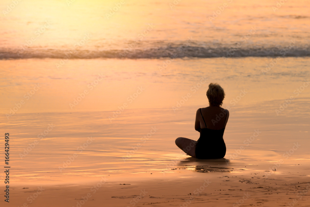 Silhouette of woman sitting on golden beach and sea bokeh at sunset..Tranquil of wonderful beach returns a freedom to your soul.