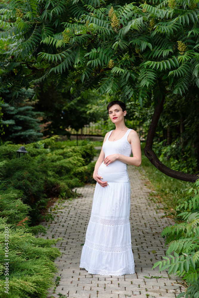 Beautiful pregnant girl in a white dress outdoors.