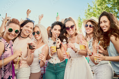 Friends posing at outdoor party while standing and drinking alcohol