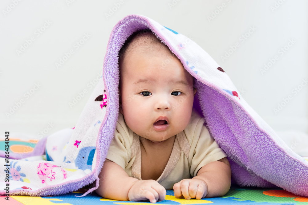 Portrait of a little adorable infant baby girl with blanket lying on the tummy on colorful eva foam indoors Portrait of a little adorable infant baby girl with blanket lying on the tummy on colorful eva foam indoors