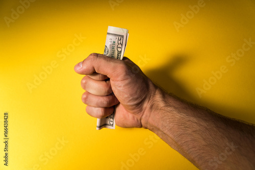 A man's hand holds out dollars. Hand and money on a yellow background. Lack of money. Family budget