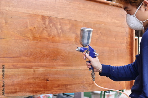 Selective focus on hands of industrial painter with safety mask painting a wooden furniture with spray gun in home workshop. Shallow depth of field. photo