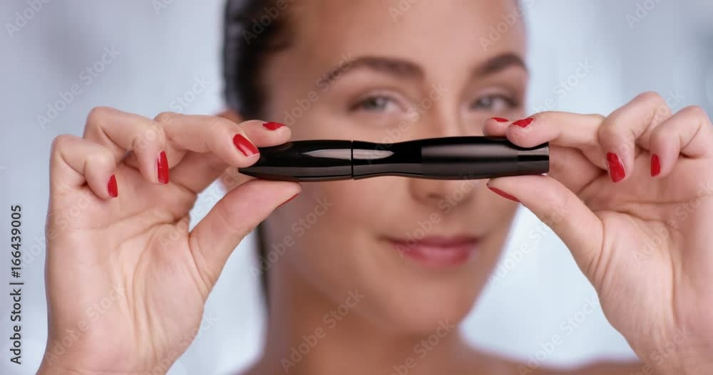 Pretty woman is showing a mascara while she looks into the camera Pretty woman is showing a mascara while she looks into the camera