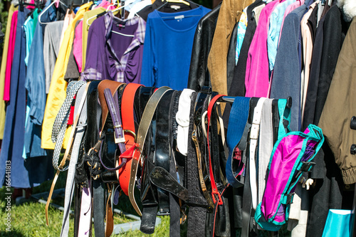 many belts and adult clothing on rack at garage sale
