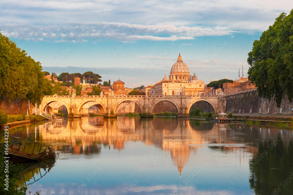 Saint Angel bridge and Saint Peter Cathedral with a mirror reflection in the Tiber River in the sunny morning in Rome, Italy.