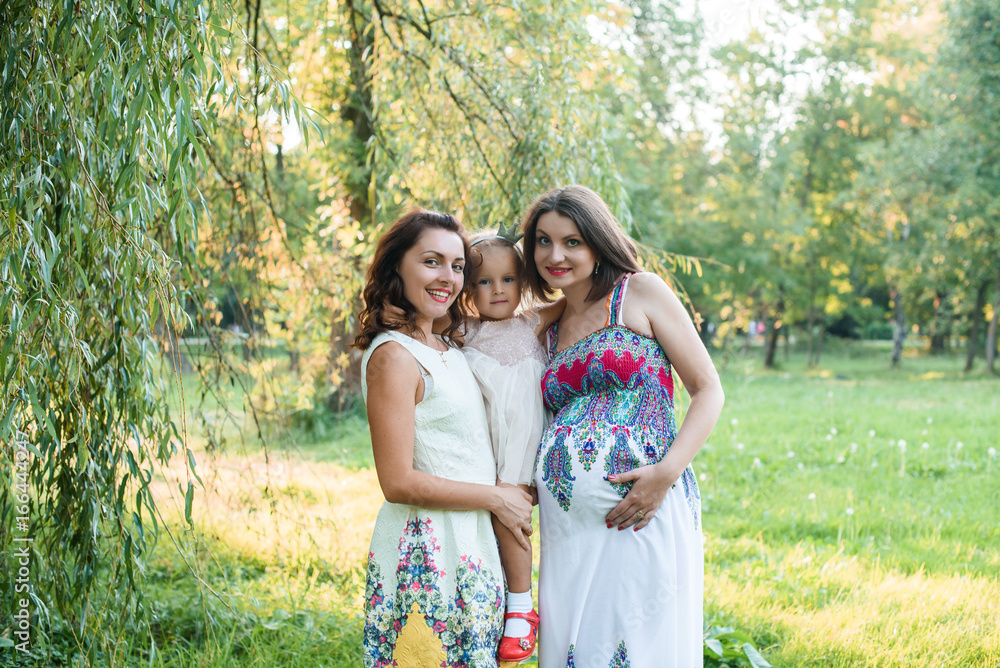 young beautiful pregnant woman walking in the park With a little daughter And sister on a sunny summer day young beautiful pregnant woman walking in the park With a little daughter And sister on a sunny summer day