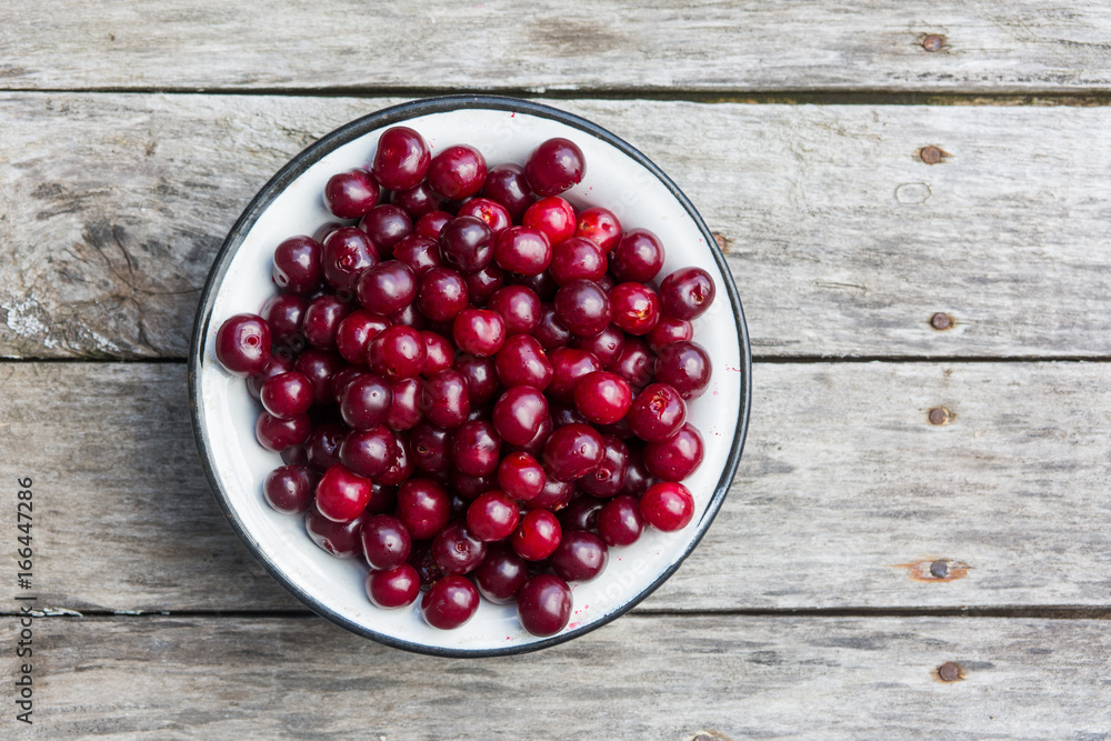 Cherry in a white bowl on a old wooden texture with rasty nails. Top view. Cherry in a white bowl on a old wooden texture with rasty nails. Top view.