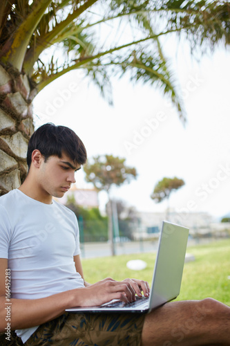 Young busy man sitting using laptop outside