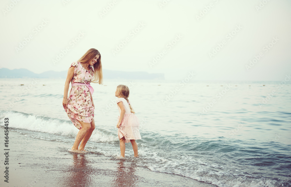 Family having fun in water on seashore. Joyful mum with little girl jumping on the beach. 