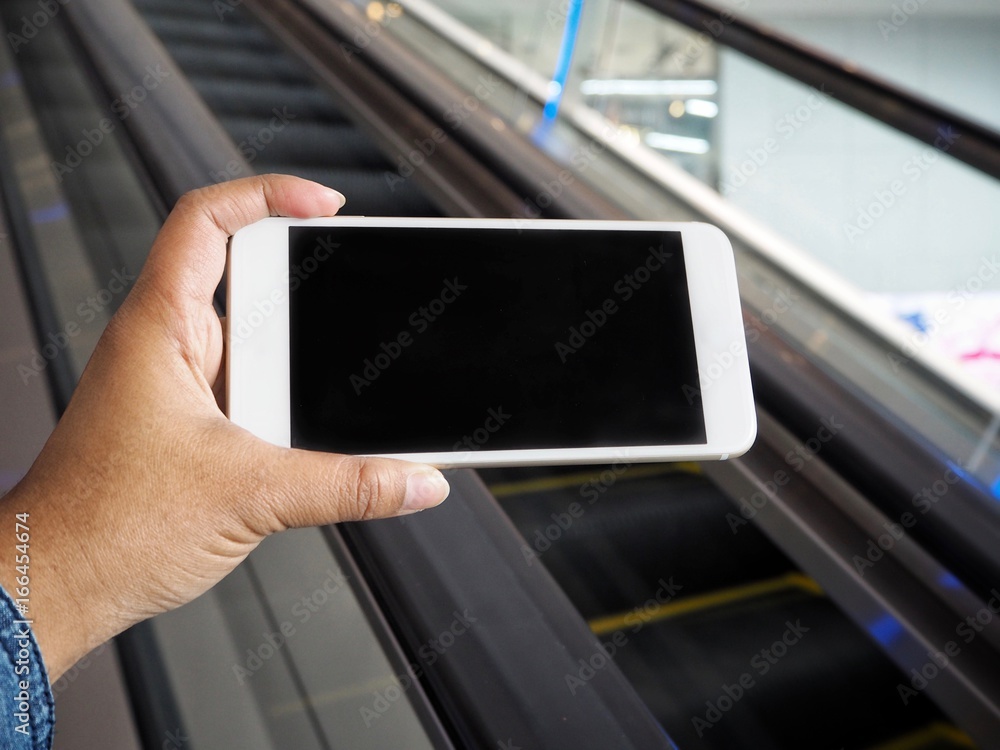Smart phone on hand with escalator at shopping mall Smart phone on hand with escalator at shopping mall
